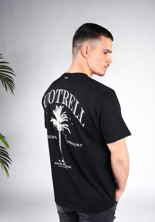 Schuin achteraanzicht van model gekleed in een heren T-shirt in zwarte kleur, met een ronde hals en een relaxed fit pasvorm. Het T-shirt is voorzien van palmboom print en de merknaam in witte kleur.
