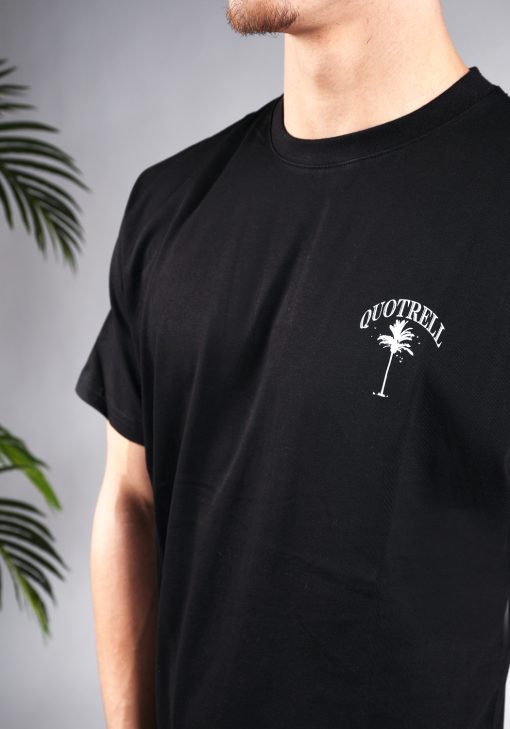 Close-up van een heren T-shirt in zwarte kleur en een ronde hals. Het T-shirt is voorzien van een subtiele palmboom en de merknaam in witte kleur op de linkerborst.