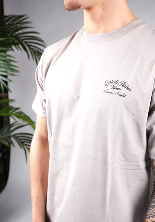 Close-up van een schuin vooraanzicht van model gekleed in een taupe T-shirt met donkere tekst op de borst.