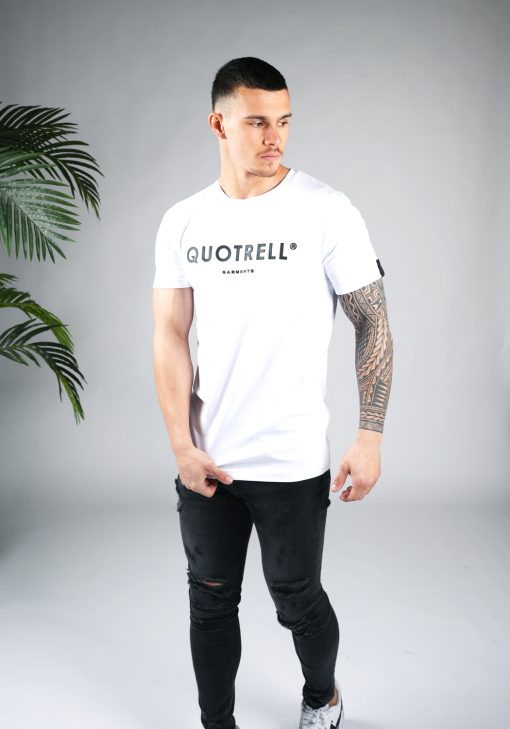 Vooraanzicht van heren T-shirt in witte kleur, met ronde hals en een slim fit pasvorm. Het T-shirt is voorzien van het QUOTRELL-logo in zwarte kleur op de borst. Het model combineert het T-shirt met een donkere jeans en witte sneakers.