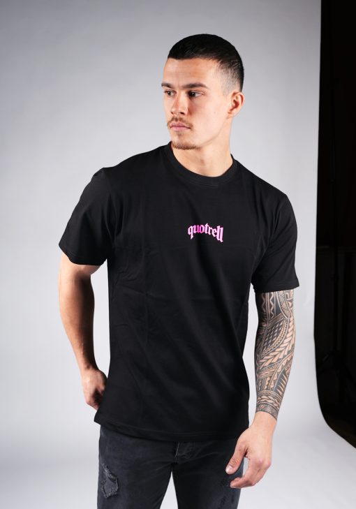 Vooraanzicht van model gekleed in een T-shirt van zwarte kleur en een relaxed fit pasvorm. Het T-shirt is voorzien van tekst in een roze neon kleur op de borst.
