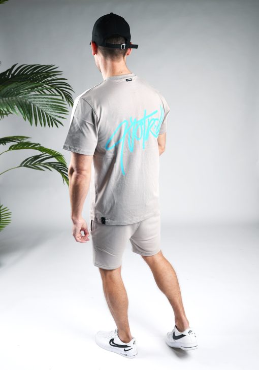 Achteraanzicht van model gekleed in grijze Quotrell set. De set bestaat uit een t-shirt met het blauwe logo op de borst en rug, en de jogger shorts met het logo op de linkerbeen.