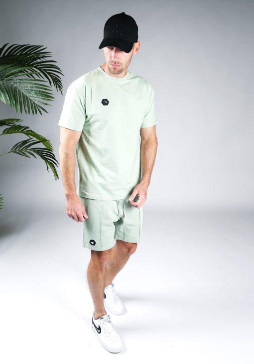 Schuin vooraanzicht van model gekleed in groene Black Bananas Hercules set. De set bestaat uit jogger shorts en een t-shirt met het Black Bananas logo badge op de borst en bovenbeen.