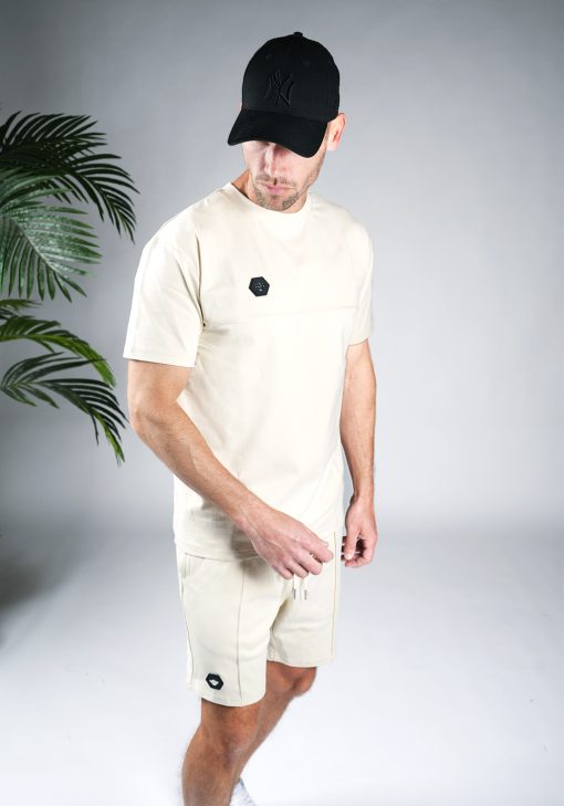 Schuin vooraanzicht van model gekleed in zandkleurige Black Bananas Hercules set. De set bestaat uit jogger shorts en een t-shirt met het Black Bananas logo badge op de borst en bovenbeen.