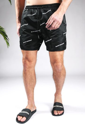 Vooraanzicht van model gekleed in zwarte black bananas swimshort. De shorts zijn voorzien van een print van de witte tekst "black bananas".