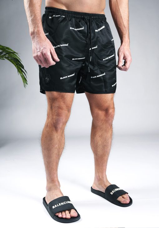 Vooraanzicht van model gekleed in zwarte black bananas swimshort. De shorts zijn voorzien van een print van de witte tekst "black bananas".