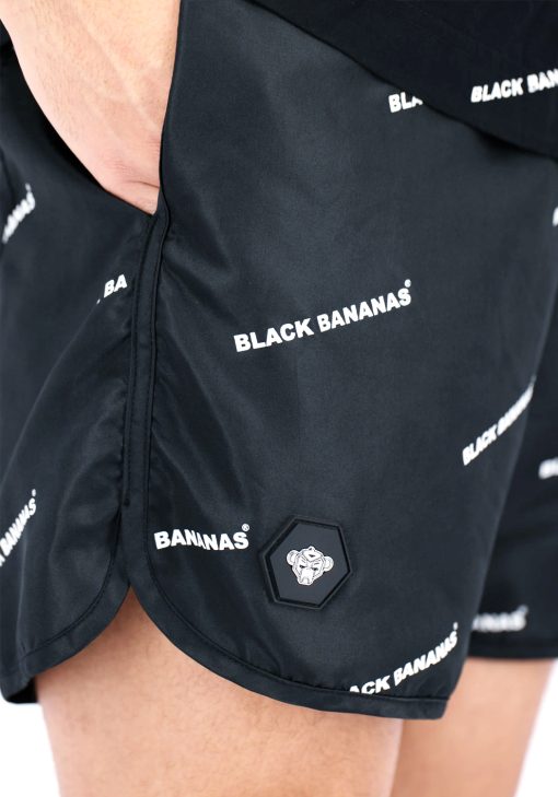 Close up van model gekleed in zwarte black bananas swimshort. De shorts hebben een print van de witte tekst "black bananas" en het black bananas logo.