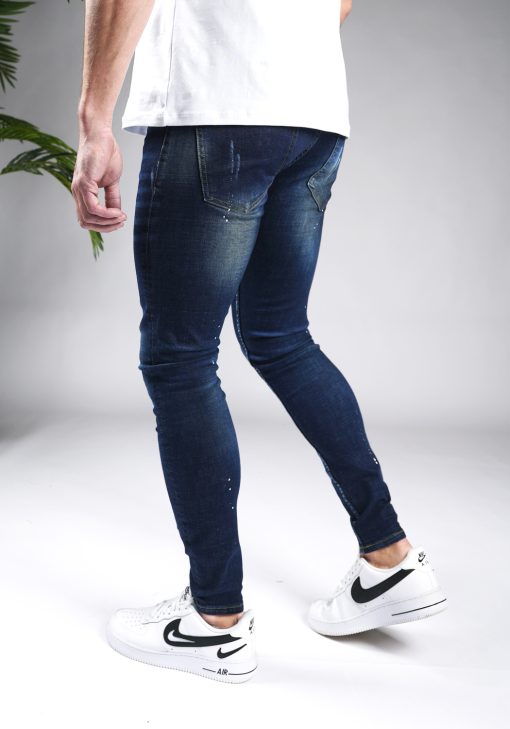 Achterkant donkerblauwe heren skinny jeans met verfspetters en damaged afwerken, gemaakt van stretch stof. Voorzien van vier zakken, knoopsluiting en riemlussen.