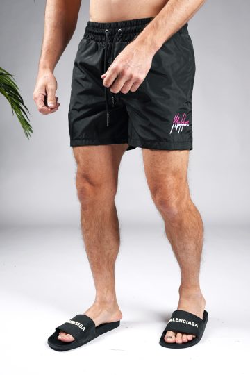 Schuin vooraanzicht van model gekleed in zwarte Malelions zwembroek met het split Malelions logo in de kleuren roze en wit op de bovenbeen en kontzak.