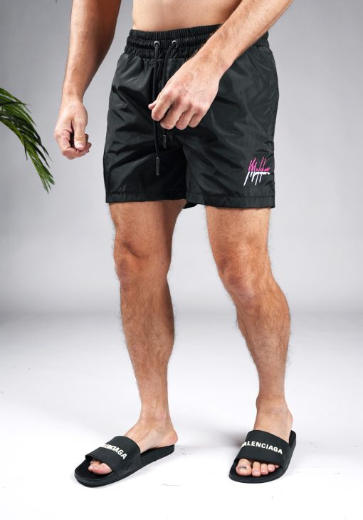 Schuin vooraanzicht van model gekleed in zwarte Malelions zwembroek met het split Malelions logo in de kleuren roze en wit op de bovenbeen en kontzak.