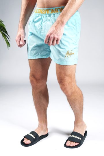 Schuin vooraanzicht onderlichaam van model gekleed in lichtblauwe Malelions zwembroek met gouden details bij de tailleband en het gouden logo op de been.