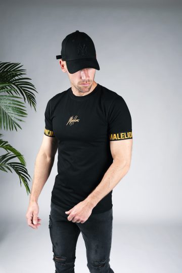 Schuin vooraanzicht van model gekleed in zwart t-shirt met het gouden Malelions logo in het midden van de borst, en de gouden tekst Malelions rondom de mouwen.
