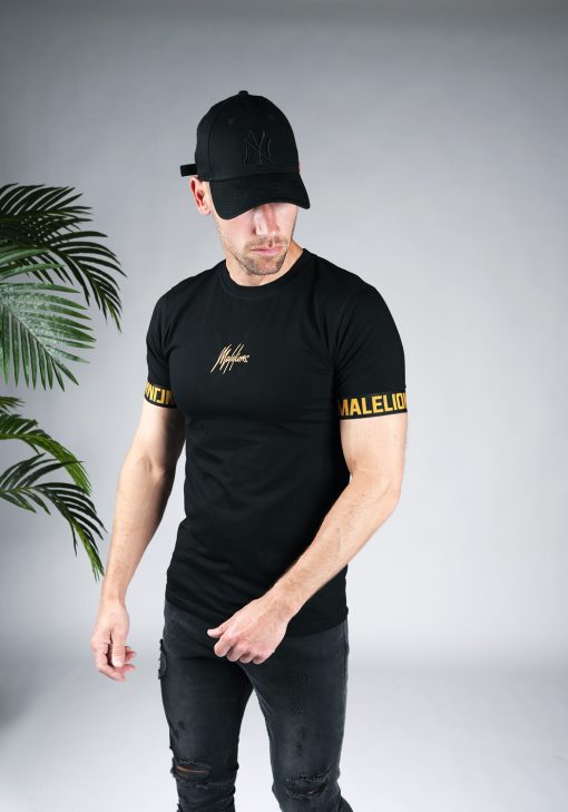 Schuin vooraanzicht van model gekleed in zwart t-shirt met het gouden Malelions logo in het midden van de borst, en de gouden tekst Malelions rondom de mouwen.