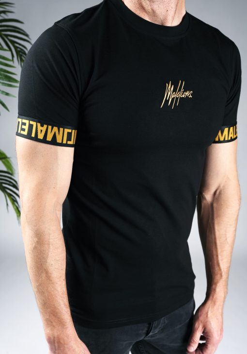 Close up vooraanzicht van model gekleed in zwart t-shirt met het gouden Malelions logo in het midden van de borst, en de gouden tekst Malelions rondom de mouwen.